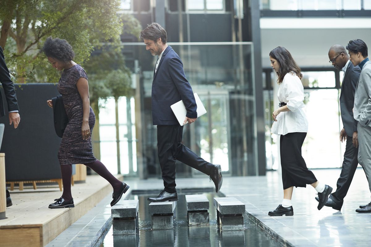 Return to office concept image showing workers entering an office building in a line.