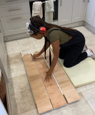 Jessica Grizzle kneeling on tiled kitchen floor and using marker pen to trace around wooden scalloped panels