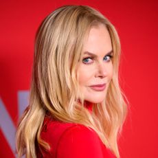 Nicole Kidman looks over her shoulder at the camera wearing a red long-sleeve dress