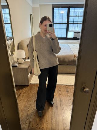 Nikki wears a tan sweater, black trousers, black ballet flats, and an ivory shoulder bag.