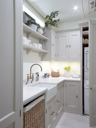 A shaker style utility room with a wicker washing basket neatly stored under the counter top and freestanding shelves
