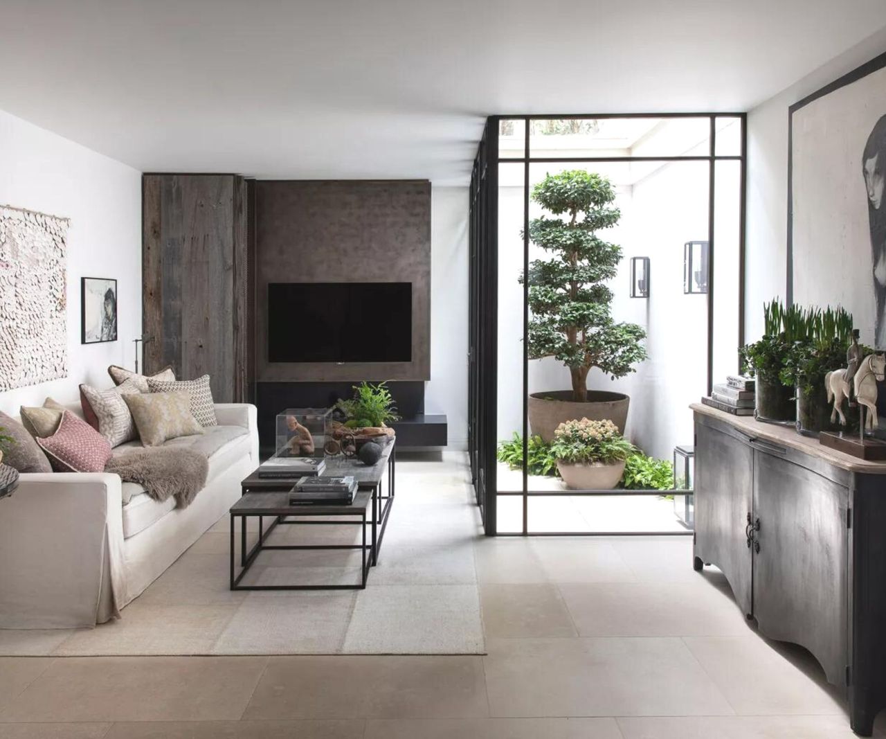 A dark, Japandi living room with a large plant feature behing glass and a TV at the far end 