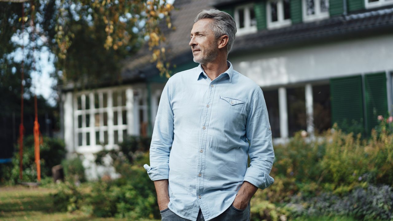 A man stands in front of his house with his hands in his pockets.