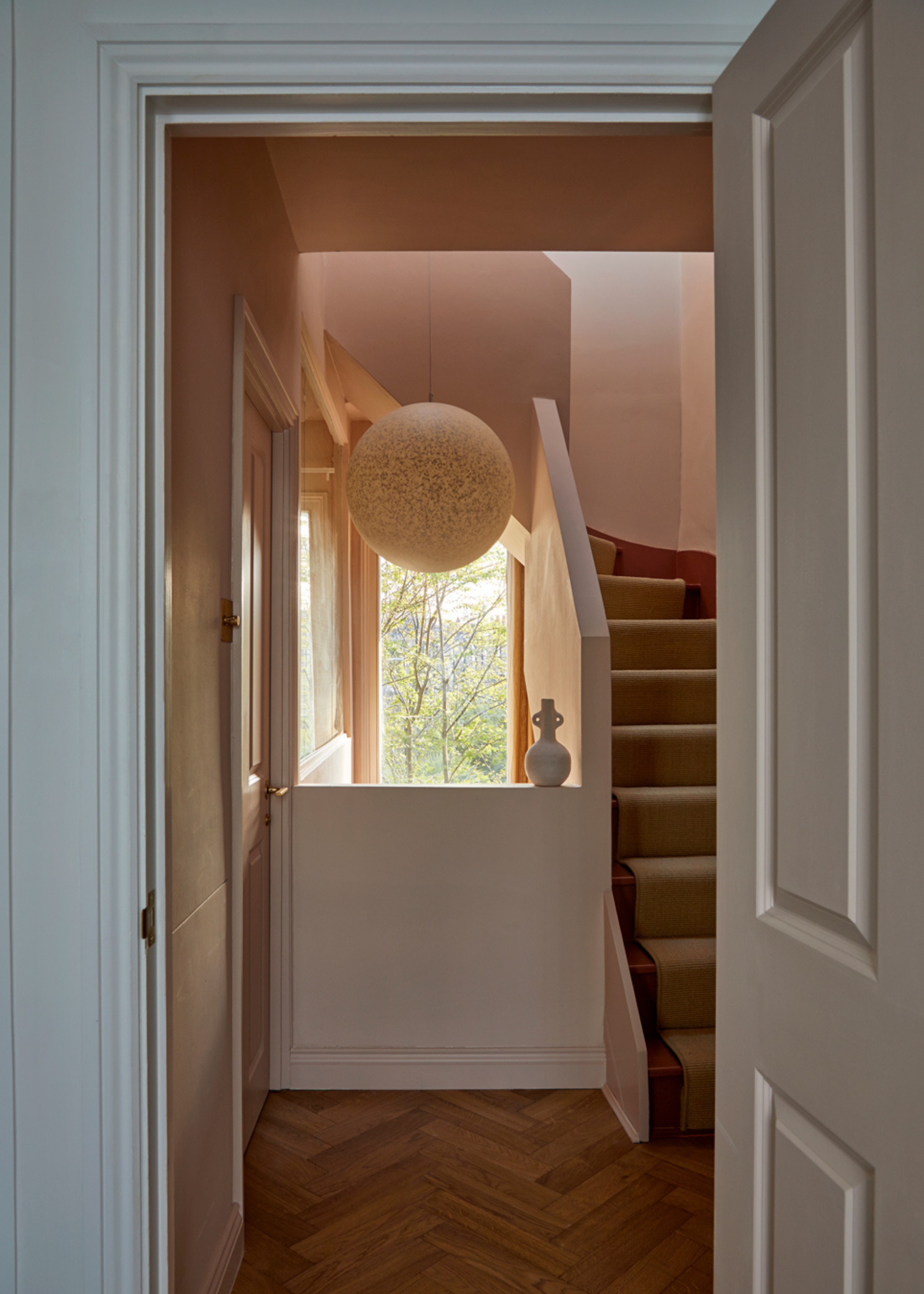 A white door leading to a staircase with a cream runner by a ledge with a vase and a pendant lamp