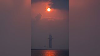 a rocket stands upright on a launch pad with the sun poking through clouds above it