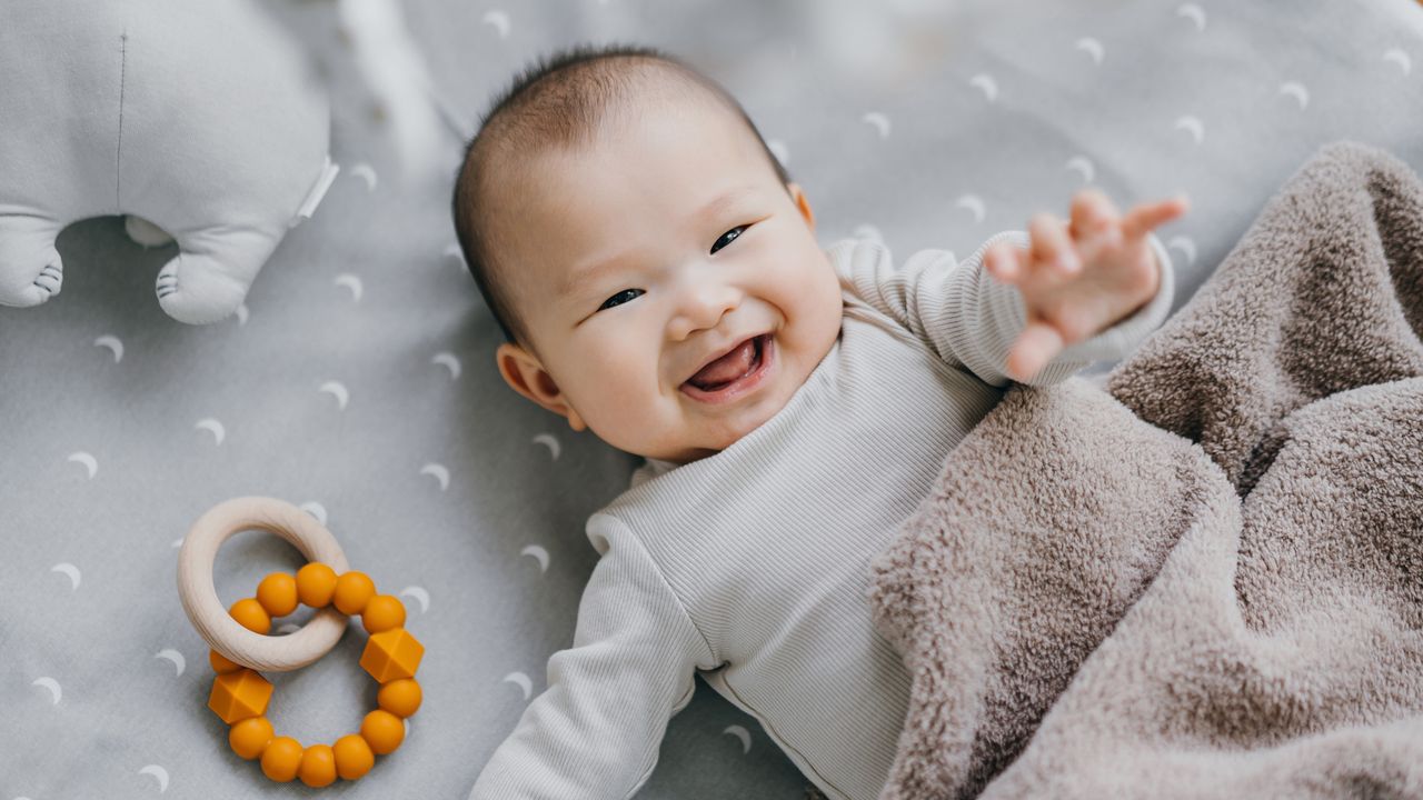 An infant smiles while lying in a crib.