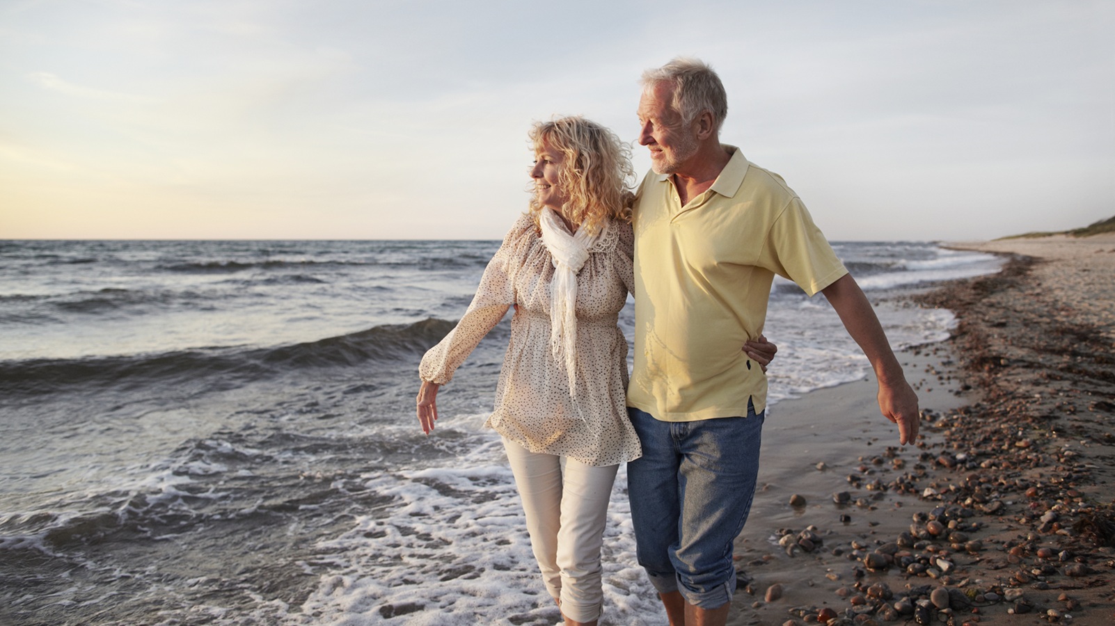 A mature couple walks on the beach.