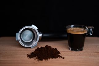 coffee grounds with a cup of espresso and an espresso machine part in the background