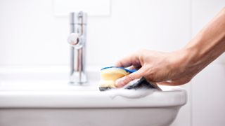 Person cleaning bathroom sink with sponge -