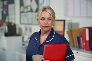 Hannah Walters as Beth Relph wearing a blue nurse's uniform and holding a red clipboard