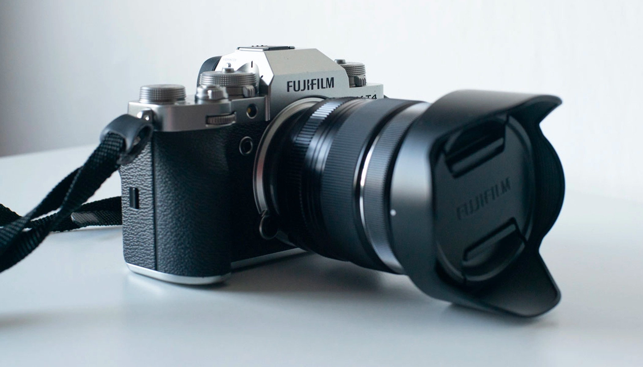 A side view of the Fujifilm X-T4, with a capped lens, resting on a white surface.