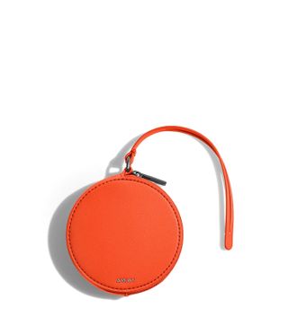 A circle zip pouch in orange leather reads "AWAY" in chrome.