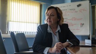 Carmen Machi in A Widow's Game, sitting in front of a whiteboard with case notes