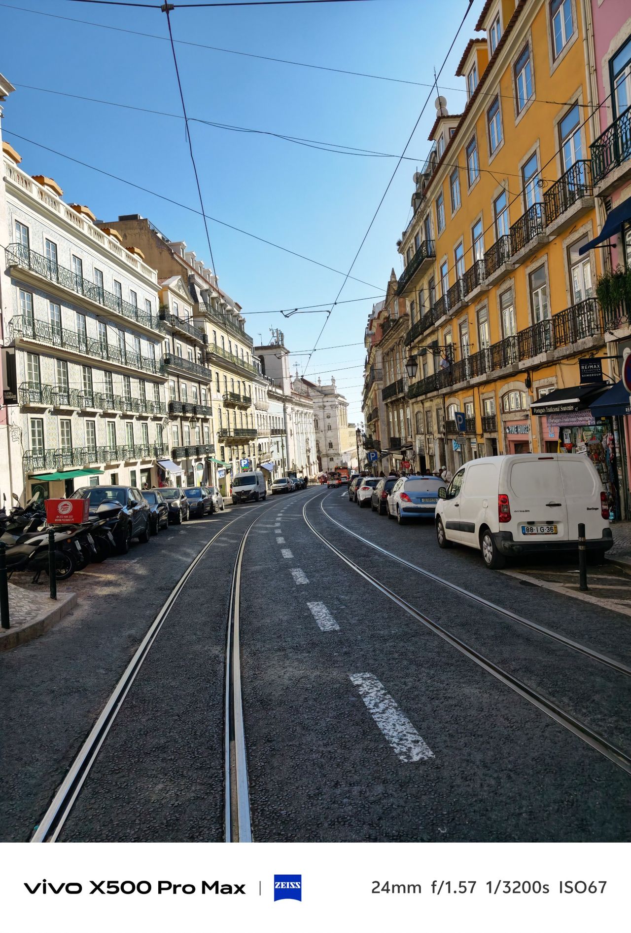 Lisbon street lined with colorful buildings, parked cars and tram tracks.