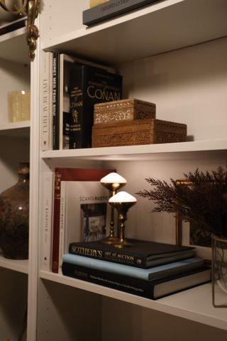 Two diamond shaped puck lights in brass candle holders on a stack of books on a bookshelf