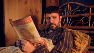 Beardy Christian David Lewis (Simon Bird) in his pyjamas in bed, looking peevishly away from his cook book towards his increasingly estranged wife in Everyone Else Burns