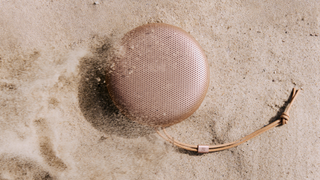 The Bang & Olufsen A1 3rd Gen in Honey Tone on a beach, with sand falling across it
