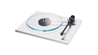 The Rega Planar 3 turntable on a plain white background without a dust cover. The record player is the white variant and it has a a transparent plinth.