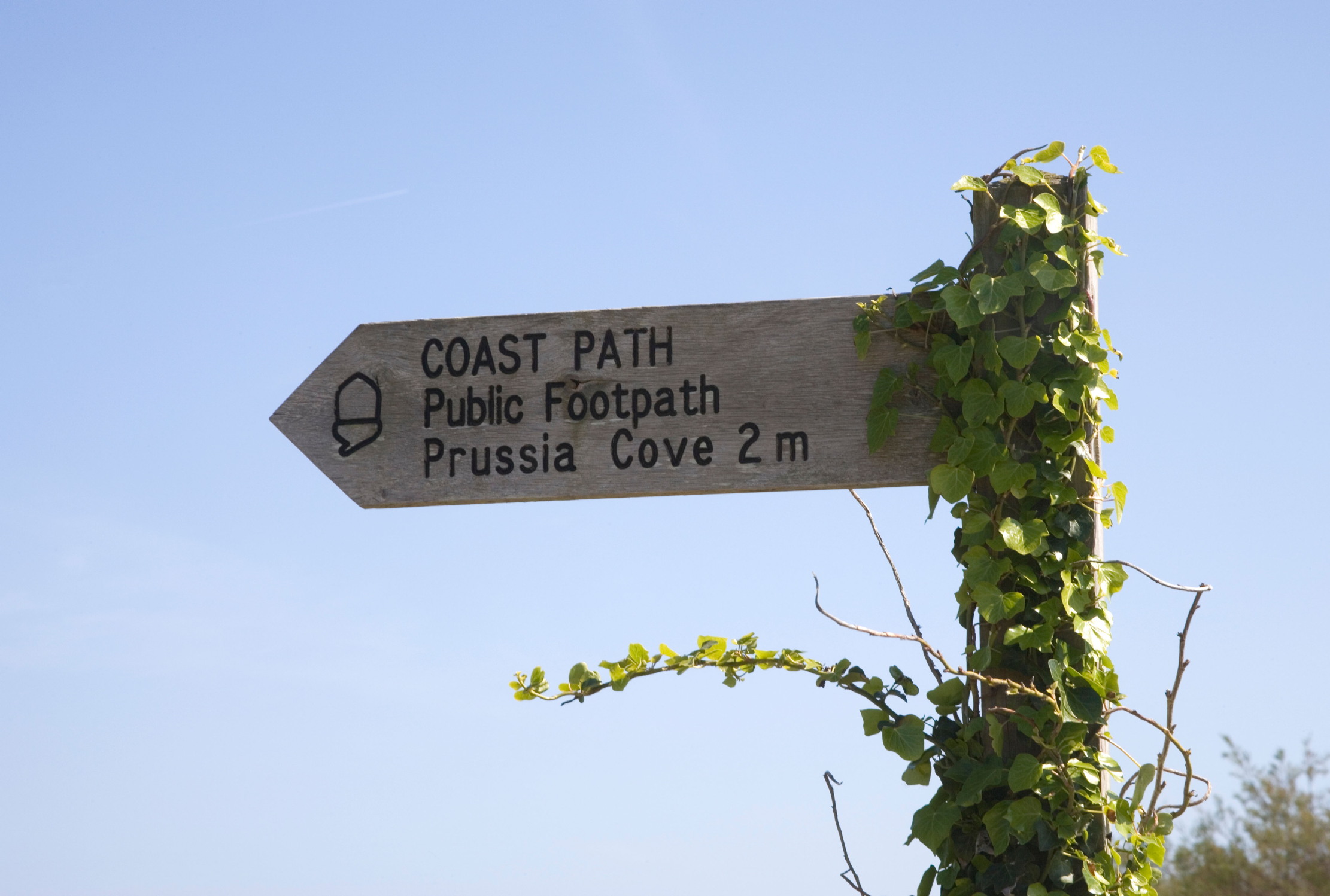A coast path sign indicating Prussia Cove is two miles away
