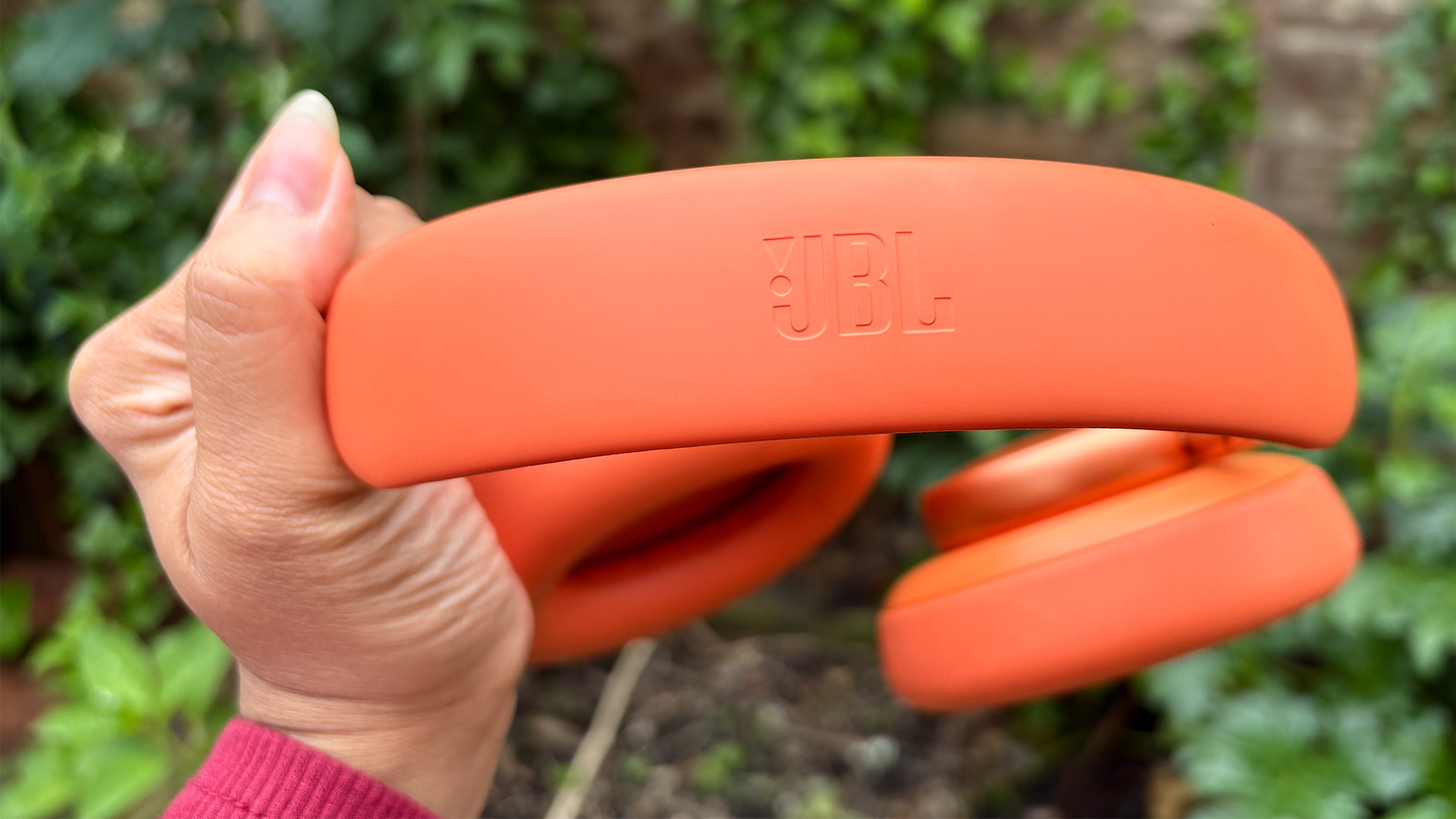 JBL Live 780NC wireless headphones held in hand in garden, detail of JBL logo etched into headband