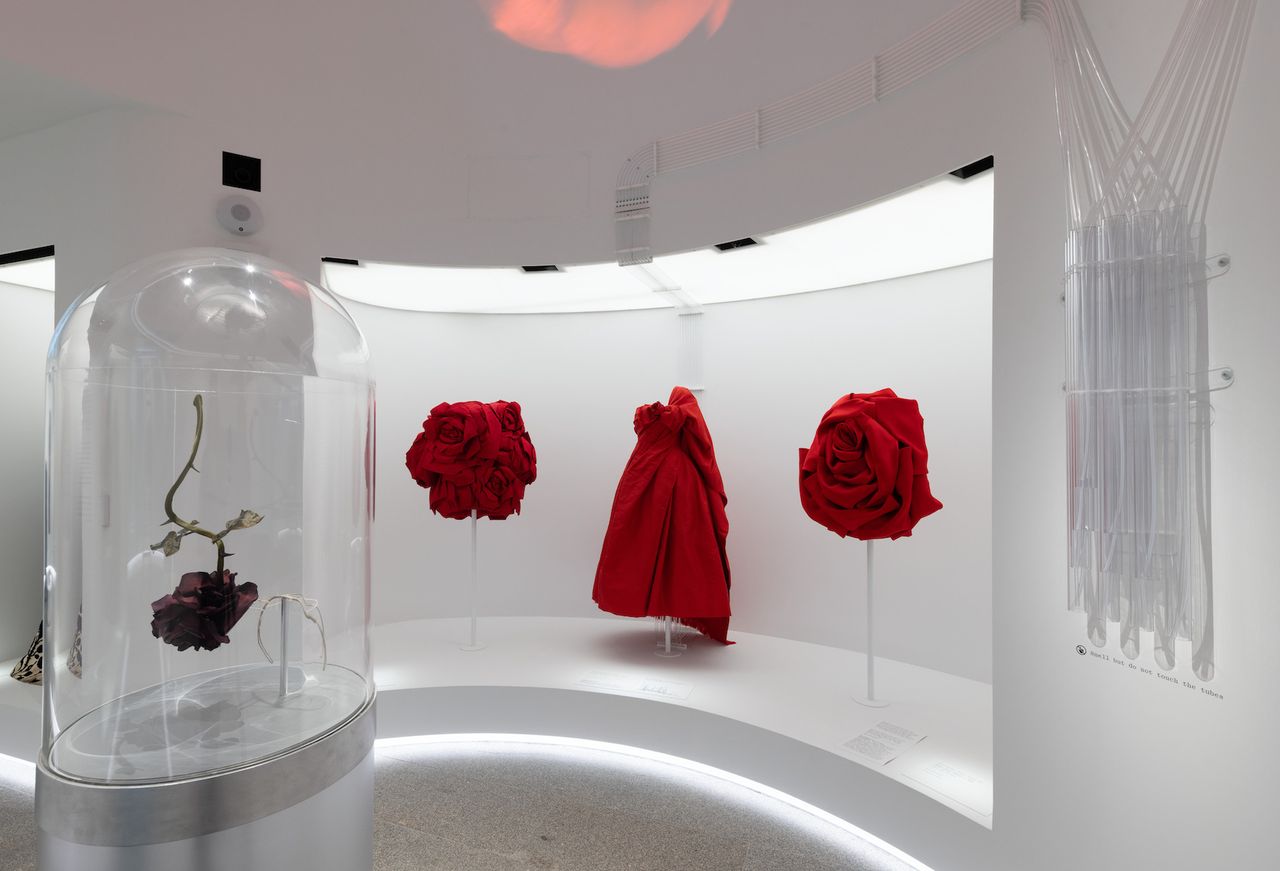 Gallery view of The Met’s Sleeping Beauties Reawakening Fashion, featuring a red dress and giant red roses in fabric in curved gallery space