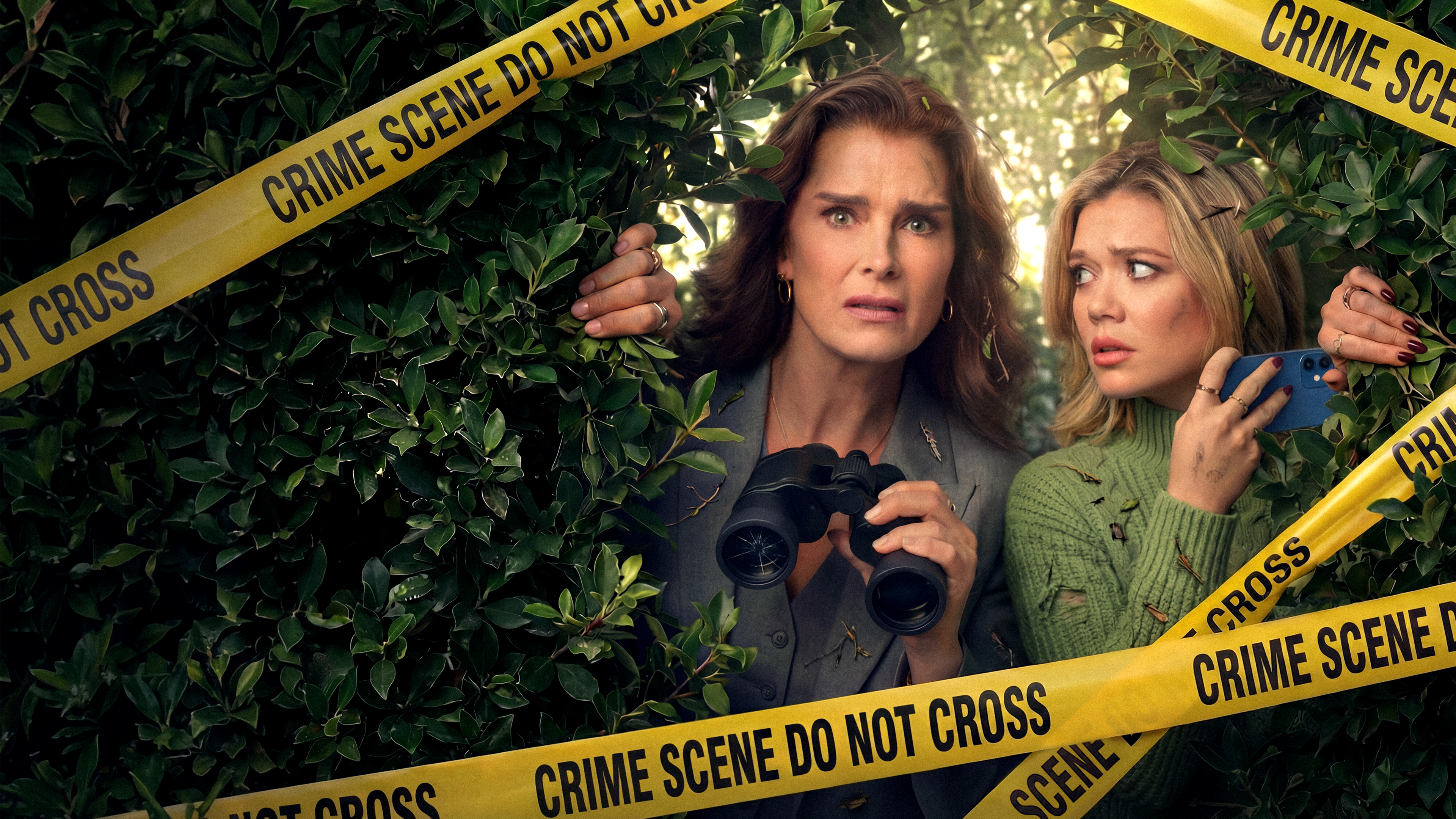 Alison Chandler (Brooke Shields) and Andrea Walker (Amalia Williamson) hiding in a bush with binoculars behind yellow crime scene tape.