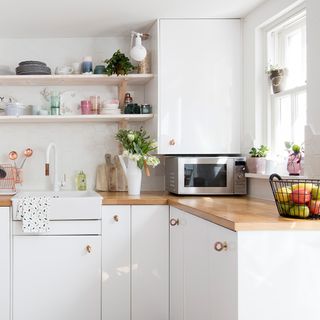 White cupboards in kitchen with wooden counter tops and a silver microwave