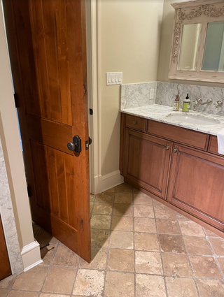 A dated bathroom with a wooden vanity and beige floor tiles