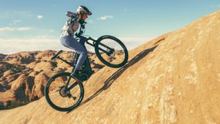 A woman rides up a steep rock slab in the desert on an e-MTB