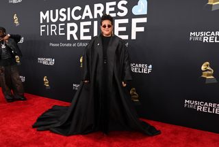 a guest at the grammys wearing a black cape with a blue heart pin