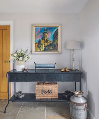 Console table in the hall with hamper basket on the lower shelf and metal milk churn on the floor.