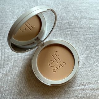 An open elf Camo Powder Foundation set against a white linen background