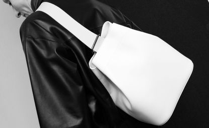 A white bag hanging off the shoulder, on the back of a person in a black leather jacket