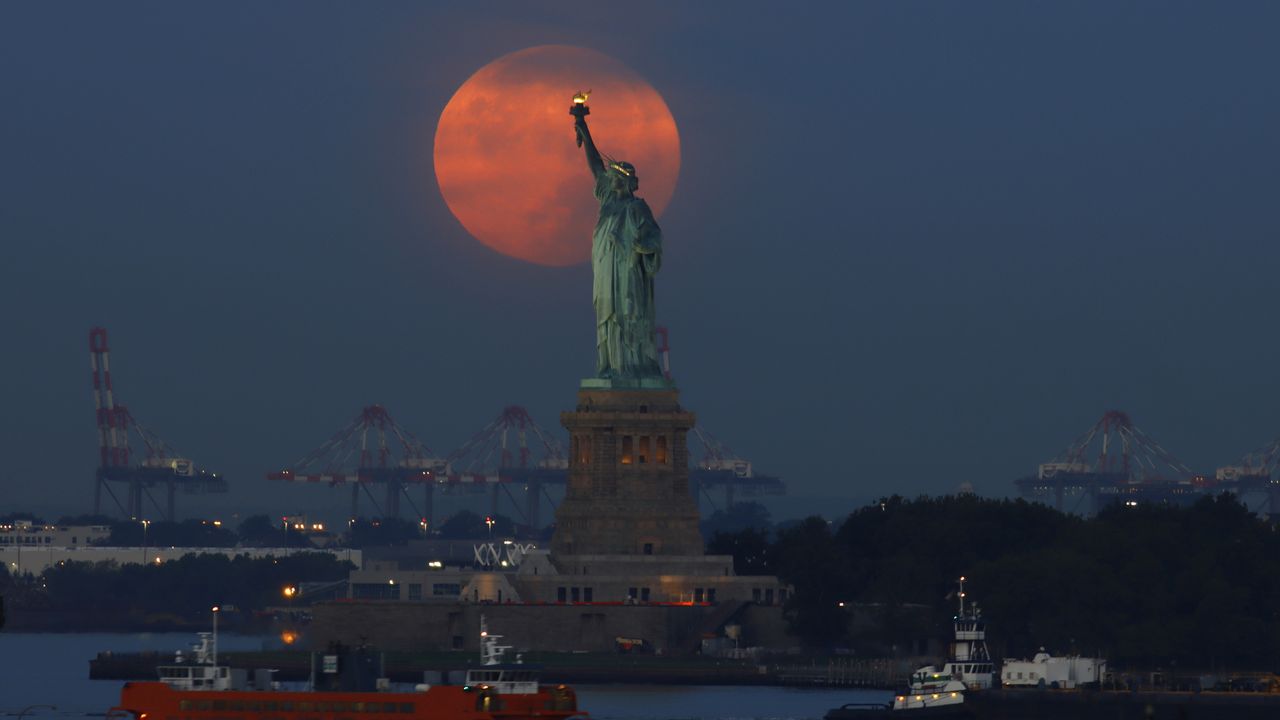 The full Harvest Moon sets behind the Statue of Liberty as the sun rises on September 10, 2022, in New York City.