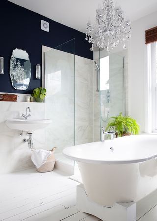 White marble shower enclosure with blue painted walls, glass chandelier, porcelain tub and painted white floor boards