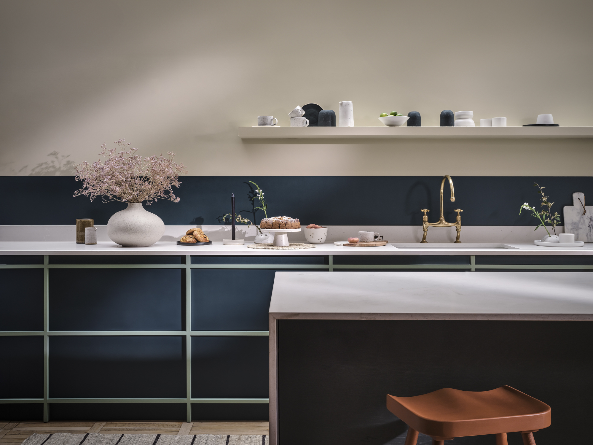 A modern style kitchen with cream coloured walls and navy and teal cupboards, with white stone work tops and kitchen island.