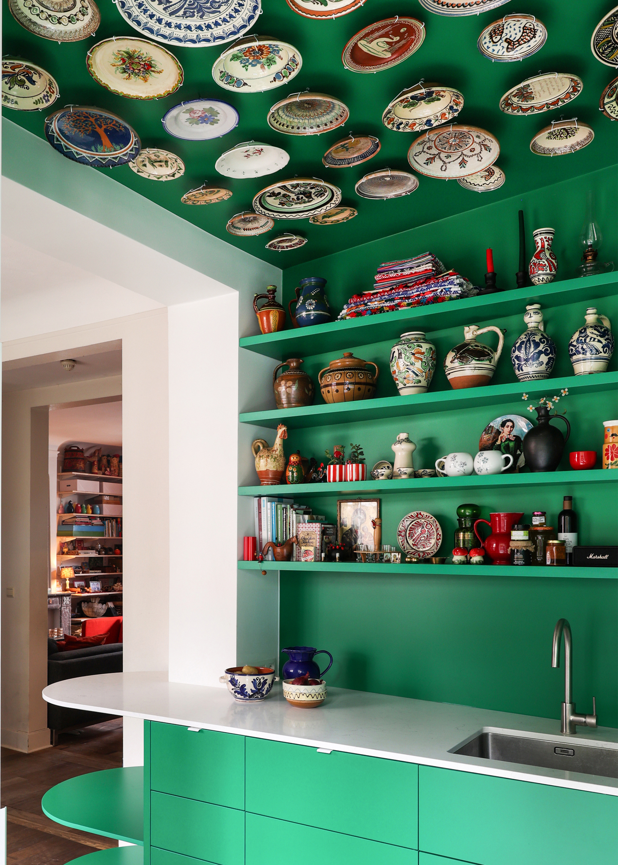a close up shot of a small green kitchen with shelves filled with a collection of pottery and art
