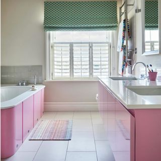 Bathroom with white floor tiles, pink double vanity unit and bathtub and green Roman blind