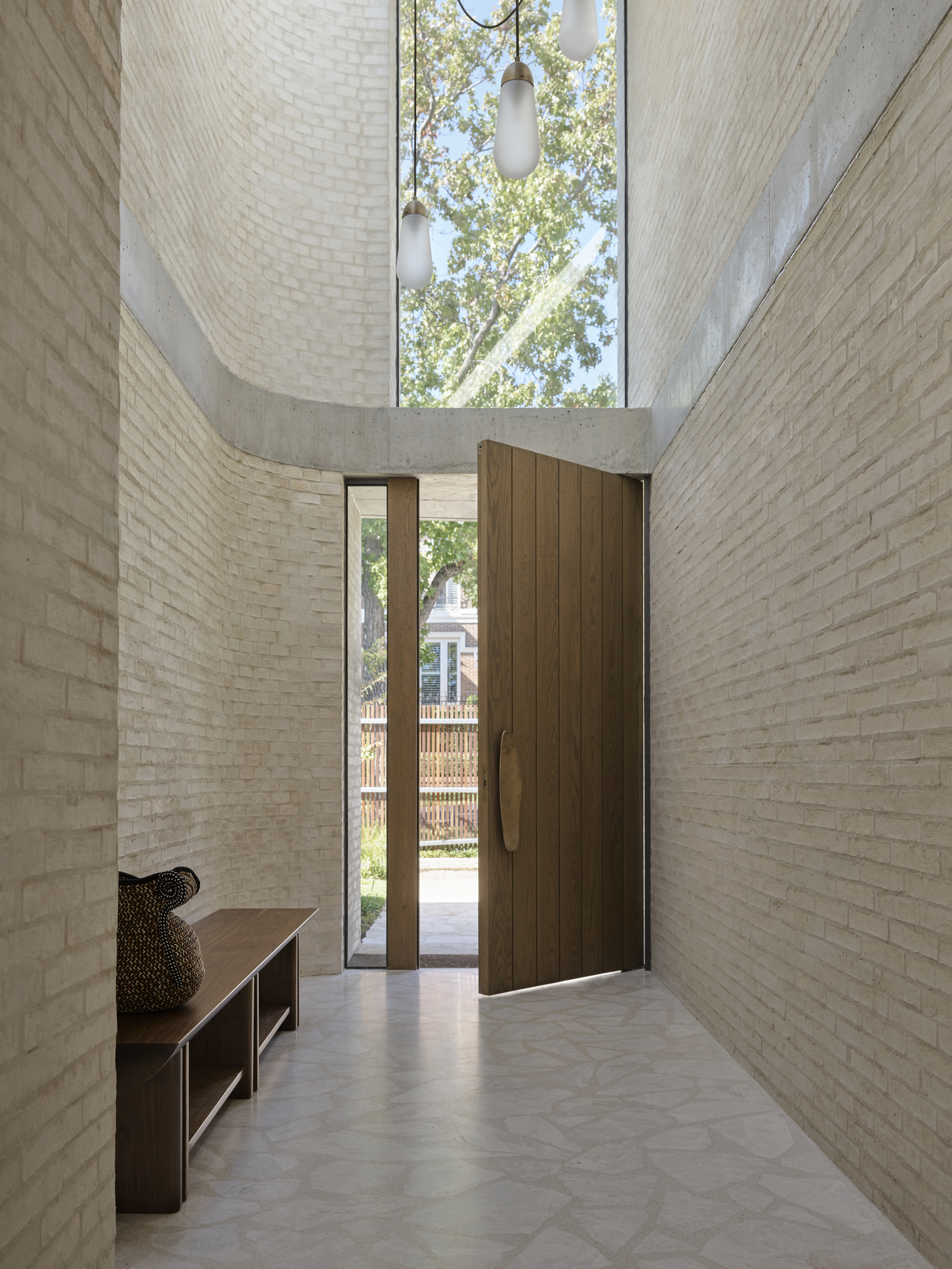bright and light entryway with double height ceiling, large timber door, timber bench seat, white palladiana flooring and blonde brick curved walls