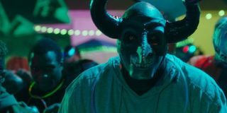 The First Purge man in a bull mask stands with an angry crowd