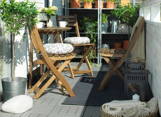 Decking tiles from Ikea with three wooden bar stools and plant pots.