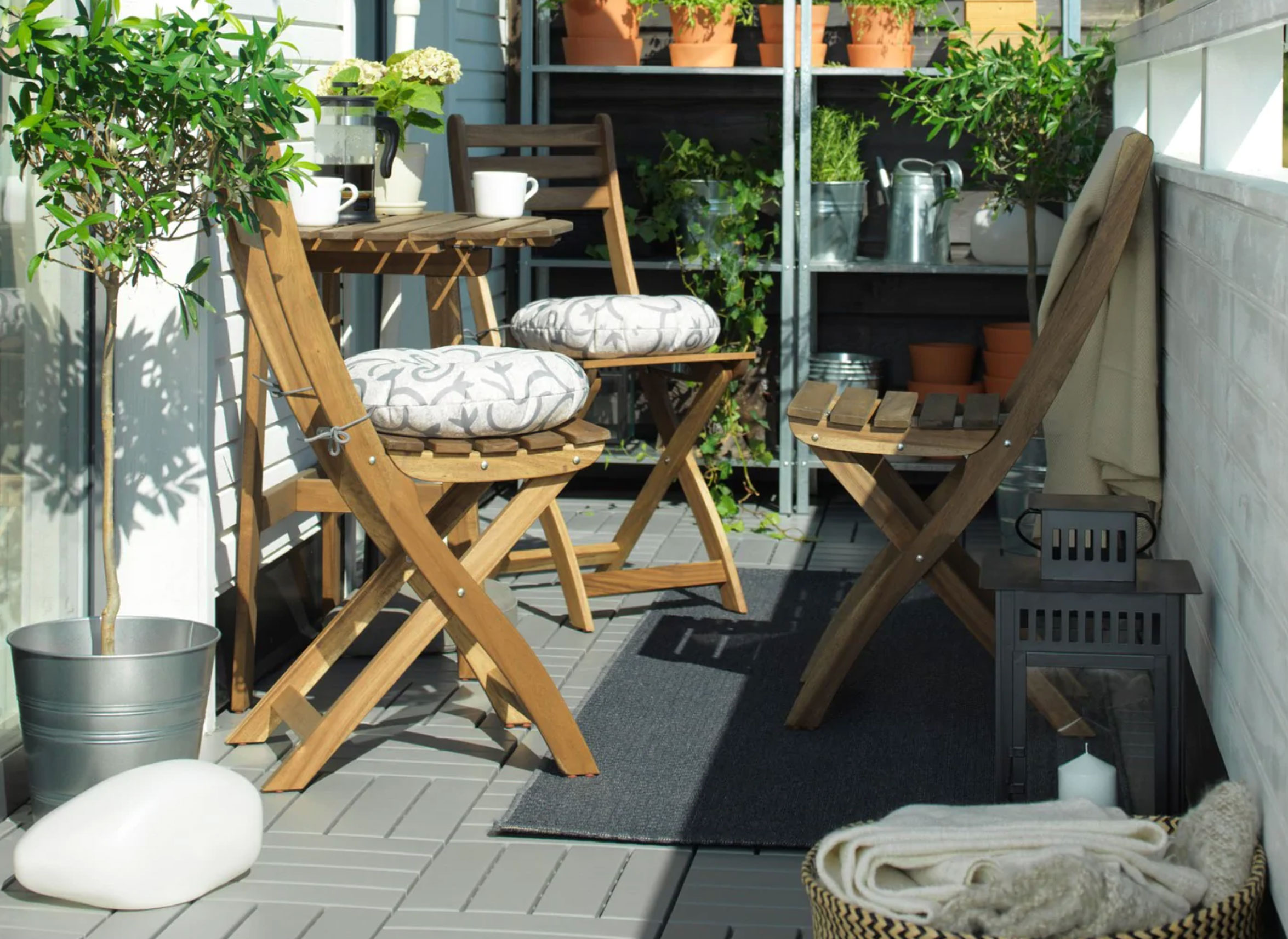 Decking tiles from Ikea with three wooden bar stools and plant pots.