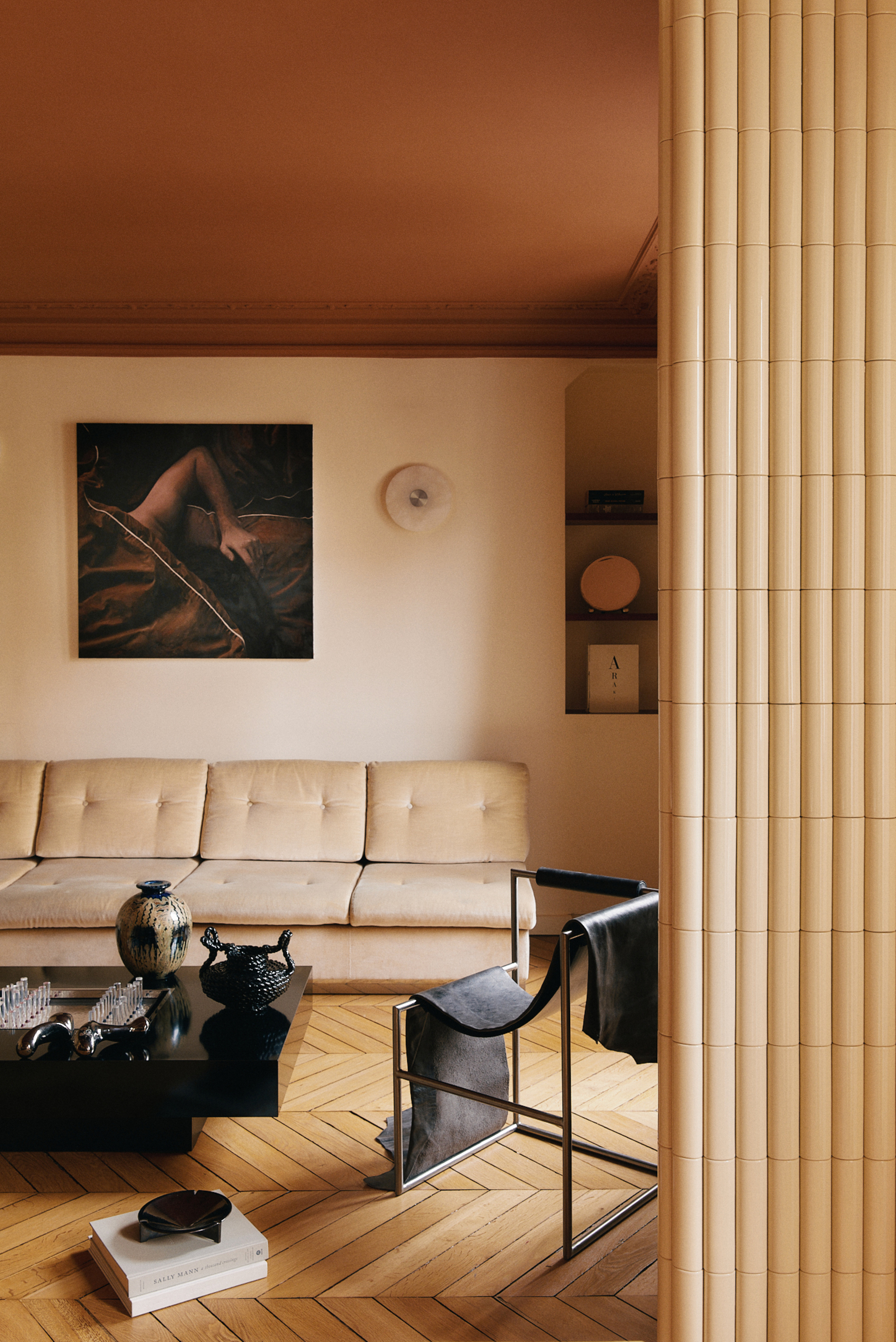 Image of a cream living room with dark burnt orange ceilings. There are herringbone wooden floors and a cream sofa with a black lacquer coffee table in front of it.