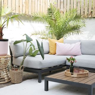 Grey outdoor sofa with yellow and pink cushions, outdoor plants
