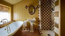 dark yellow green panelled bathroom with a brown and cream checkerboard tiled shower and a freestanding bathtub with a traditional pedestal sink