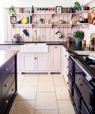 kitchen with belfast sink and pink Shaker style cabinets and dark blue island and range cooker in 12th century Cotswolds country house