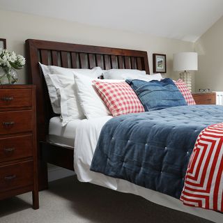 Bedroom with wooden bedroom furniture and red, whit and blue cushions and bedspread