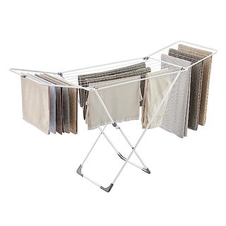 A large white metal drying rack with fold-out wings, with laundry hanging from it