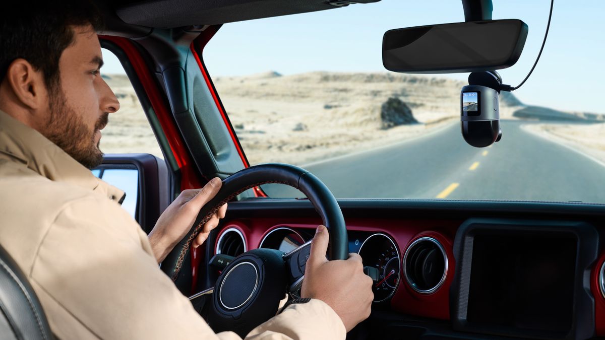 70mai 4K Omni dash cam in front of car below the rear view mirror as a person drives down road in desert-like environment