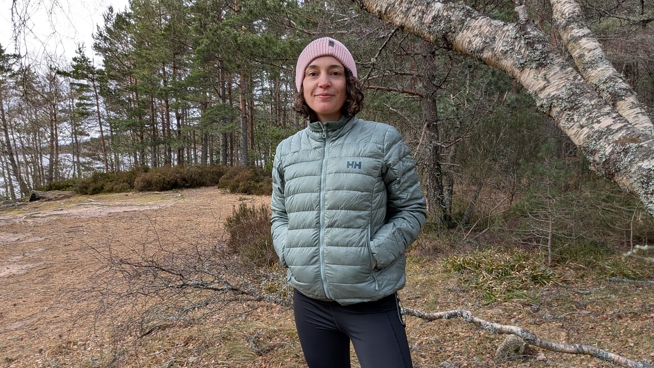 A woman on a beach wearing a green down jacket with hands in pockets